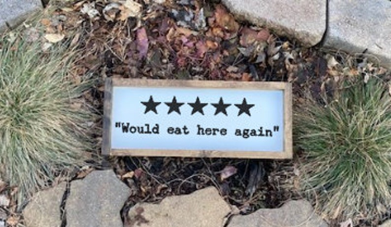 May include: A rustic wooden sign with a white background and black text. Five black stars are displayed above the text "Would eat here again".