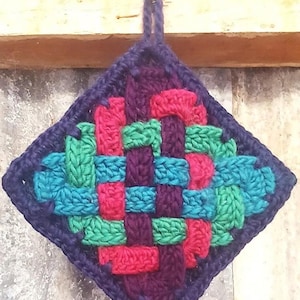 May include: A handmade, square crochet potholder with a woven design. The potholder features a dark blue border and a colorful woven pattern of teal, green, pink, and purple yarn. A loop is attached for hanging.
