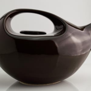 以下が含まれることがあります： 光沢のあるダークブラウンの陶器製ティーポット。丸みを帯びた膨らみのある本体に、上部でアーチを描く一体型のハンドルが付いています。側面には短い先細りの注ぎ口があり、上部中央には円形の蓋が備わっています。