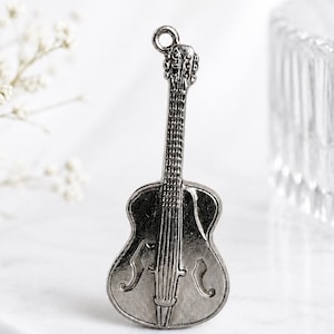 Puede incluir: Un dije de metal en tono plateado con forma de guitarra, que presenta un diapasón detallado, un puente y dos aberturas en forma de f en el cuerpo. El dije incluye un pequeño lazo circular en la parte superior para sujetarlo, con acabado pulido.