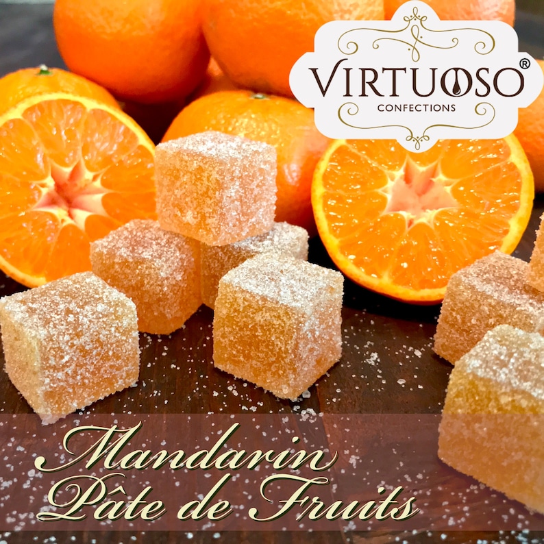 May include: Mandarin Pate de Fruits by Virtuoso Confections. Orange flavored jelly candies dusted with sugar crystals, arranged on a wooden surface with fresh mandarin oranges.