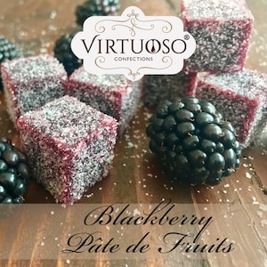 May include: Blackberry Pate de Fruits by Virtuoso Confections.  A close-up of a square, red, jelly-like candy dusted with sugar.  The candy is surrounded by blackberries and other candies.