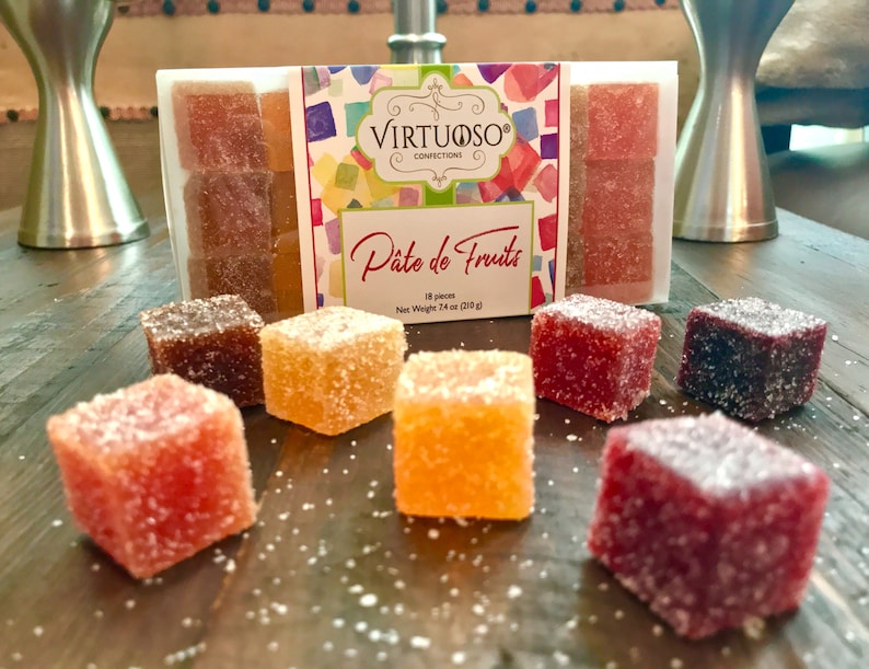 May include: A box of assorted fruit flavored jelly candies called "P&acirc;te de Fruits" by Virtuoso Confections. The box contains 18 pieces and weighs 7.4 oz (210 g). The candies are arranged in a square shape and are dusted with sugar crystals.