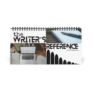 May include: A white spiral bound notebook with the text "the WRITER'S REFERENCE" and the website "www.thewritingshop.store". The notebook is open to a blank page with a pen on it. The notebook is on a wooden surface. There is a laptop computer and other writing supplies in the background.