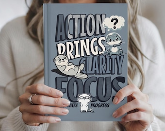 May include: A gray journal with the words "ACTION BRINGS CLARITY FOCUS" in a bold, playful font. The cover features cartoon otters and a question mark. The phrase "...CREATES PROGRESS" is also visible.