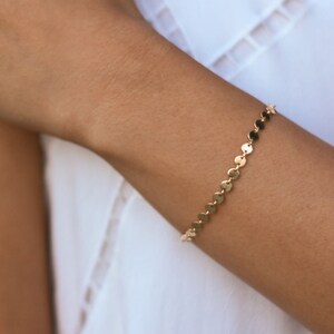 May include: A gold chain bracelet with small, round links. The bracelet is on a person's wrist.