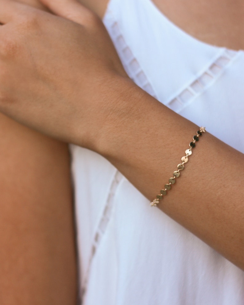 May include: A gold chain bracelet with small, round links. The bracelet is on a person's wrist.