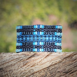 May include: A blue and black beaded bracelet with a geometric pattern. The bracelet is made with small, round beads in shades of blue and black, creating a visually appealing design.