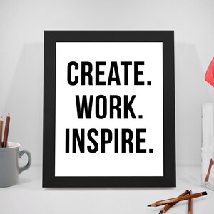 Könnte beinhalten: Schwarz gerahmter Druck mit dem Text "CREATE. WORK. INSPIRE." auf weißem Hintergrund. Der Druck befindet sich auf einer weißen Oberfläche mit einer grauen Tasse und Bleistiften sowie einer roten Blume in einer durchsichtigen Glasvase.