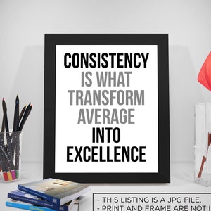 Puede incluir: Una impresión enmarcada en negro con el texto "CONSISTENCY IS WHAT TRANSFORM AVERAGE INTO EXCELLENCE". La impresión está sobre un fondo blanco y está sentada sobre una mesa con un jarrón de flores rojas y un vaso de lápices.