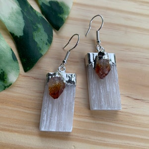 May include: A pair of silver earrings with white selenite crystal and a small orange citrine point hanging from each.