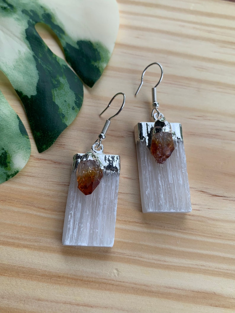 May include: A pair of silver earrings with white selenite crystal and a small orange citrine point hanging from each.