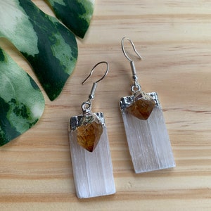 May include: A pair of silver earrings with a white selenite stone and a brown citrine crystal. The earrings are rectangular in shape and have a silver hook.