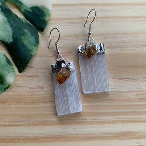 May include: A pair of silver earrings with white selenite crystal and a small amber stone. The earrings are rectangular in shape and have a silver hook.