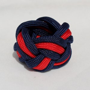 May include: A red and navy blue braided knot, tied in a complex pattern, resembling a small ball.