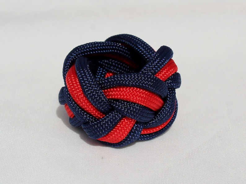 May include: A red and navy blue braided knot, tied in a complex pattern, resembling a small ball.