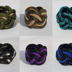 May include: Six different colored knotted rope balls. The balls are made of braided rope and are in various camouflage patterns, including green, brown, blue, black, and purple.