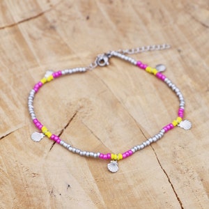 Peut inclure: Un bracelet de cheville en argent avec des perles roses et jaunes et des breloques en forme de coquillages argentés.
