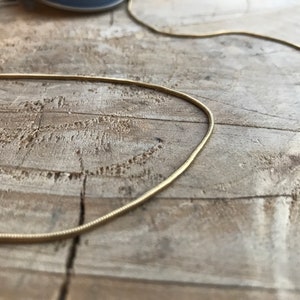May include: A gold snake chain necklace on a wooden surface.