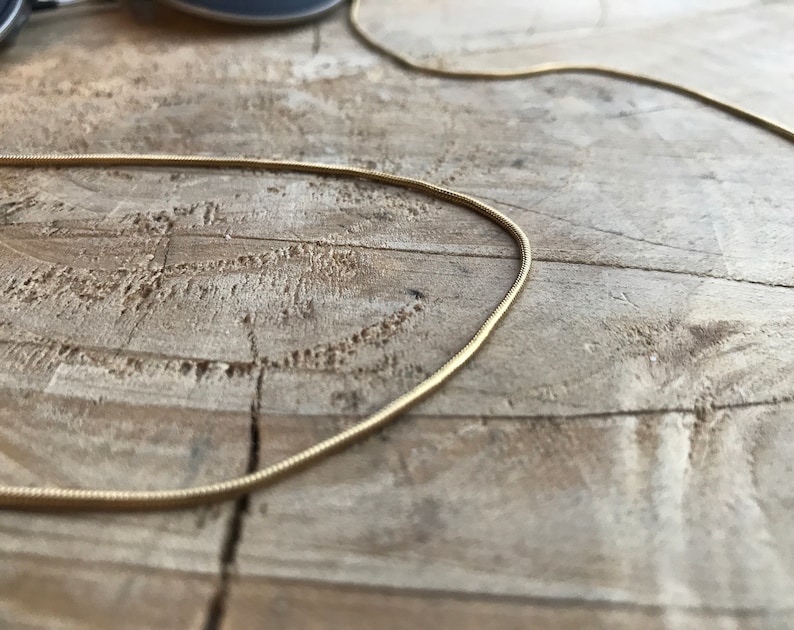 May include: A gold snake chain necklace on a wooden surface.