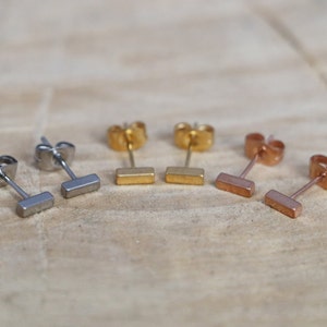 May include: Three pairs of bar stud earrings in silver, gold, and rose gold.