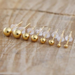 May include: A set of eight gold ball stud earrings of varying sizes. The earrings are displayed on a wooden surface.