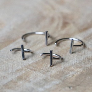 Può includere: Tre orecchini a cerchio in argento con un design a barra verticale. Gli orecchini sono realizzati in metallo sottile e hanno uno stile semplice e minimalista.