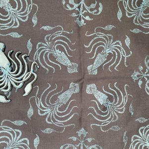 May include: A brown fabric with a repeating pattern of stylized squid in light blue. A separate light blue squid-shaped object is on the left. The design has a nautical or marine theme.