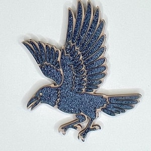 May include: A wooden raven cutout in flight, featuring a textured navy blue finish. The bird's wings are spread, and its beak is open. The edges of the raven are a light brown color.