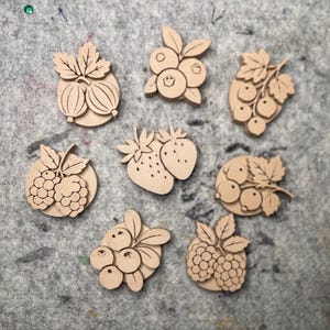 May include: A collection of eight light-colored wooden buttons, each featuring a laser-cut design of various fruits including strawberries, raspberries, blueberries, gooseberries, and currants, with detailed leaf and berry textures.