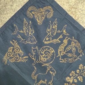 May include: Dark blue fabric with gold-colored zodiac and nature-inspired designs. The fabric features images of a ram, fish, cat, goat, and other decorative elements. The designs are evenly spaced across the fabric.