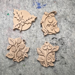 May include: Four light tan, flat, decorative relief ornaments featuring botanical designs. One shows holly leaves and berries, another displays raspberries on a vine, a third depicts blackberries on a stem, and the fourth shows blueberries on a branch.
