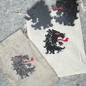 May include: The image showcases a collection of items featuring a stylized wolf design. Two wooden wolf head cutouts, one gray and one black, are displayed alongside two small drawstring bags. One bag is beige with a wolf graphic, and the other is white.