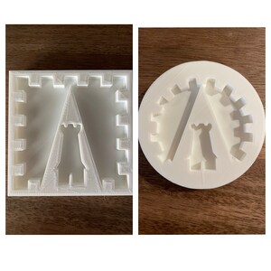 May include: Two white 3D-printed molds. One is square with a castle design and a central tower. The other is circular, featuring a gear-like border and a similar tower design. Both are on a wooden surface.