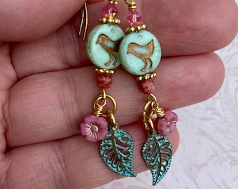 May include: Teal and gold earrings with a turquoise bird charm, pink flower accents, and a leaf design.