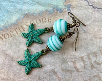 May include: Teal starfish dangle earrings with white and teal striped glass beads. The earrings have bronze-colored hooks.