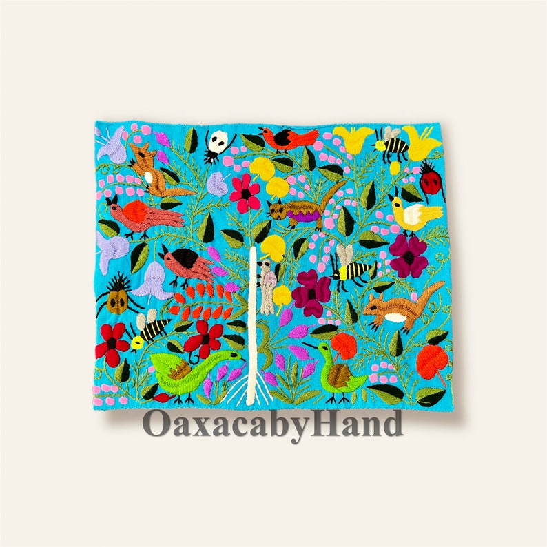 K&ouml;nnte beinhalten: Ein lebendiges, besticktes Textil mit t&uuml;rkisfarbenem Hintergrund und farbenfroher Flora und Fauna. Das Design umfasst V&ouml;gel, Bienen, Blumen und andere Kreaturen. Der Text "OaxacabyHand" ist unten sichtbar.