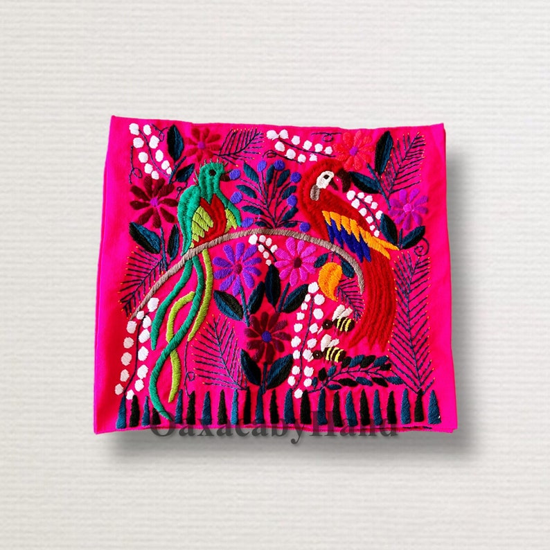 K&ouml;nnte beinhalten: Ein leuchtend pinkfarbenes Textil mit aufwendiger Stickerei von zwei bunten V&ouml;geln auf einem Ast, umgeben von Blumen und Bl&auml;ttern. Der Text "OaxacabyHand" ist unten eingestickt. Die V&ouml;gel sind gr&uuml;n und rot.
