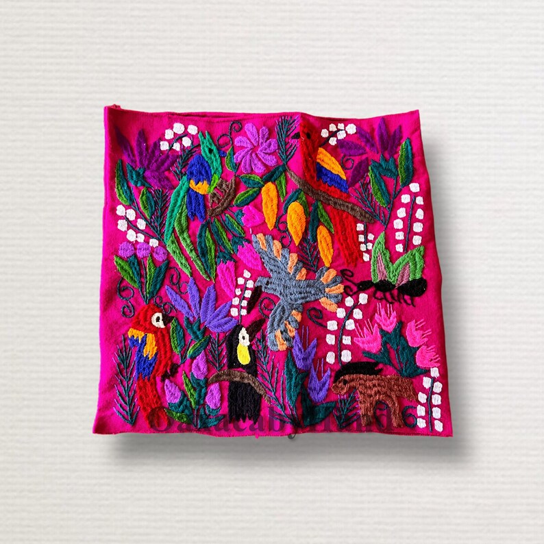 K&ouml;nnte beinhalten: Ein lebendiges, besticktes Textil mit einer farbenfrohen Dschungelszene. Das Design umfasst Papageien, Tukane und andere V&ouml;gel inmitten &uuml;ppigen Blattwerks und Blumen, alles vor einem hellrosa Hintergrund.