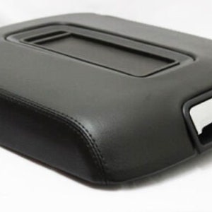 May include: Black leather center console armrest with a storage compartment and a small cutout on the side.