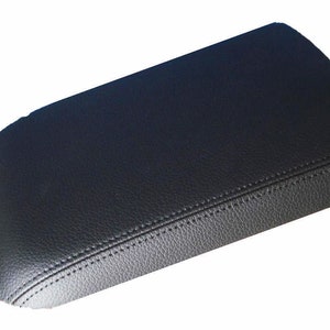 May include: Black leather center console armrest cover with a stitched seam.