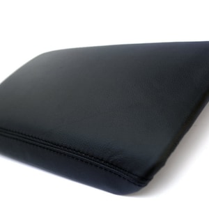 May include: Black leather center console armrest cover with a stitched seam.