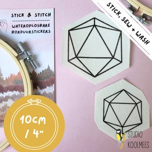 May include: Two white fabric patches with black geometric designs, resembling a 3D shape. The patches are labeled "Stick, Sew + Wash" and are 4 inches in diameter. The patches are on a pink background.