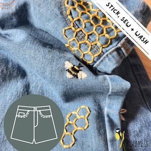 Może przedstawiać: Zbliżenie jasnoniebieskich szortów dżinsowych z haftowanymi detalami. Zawiera żółty wzór plastra miodu i pszczołę. Widoczny jest tekst "STICK, SEW + WASH". Grafika szortów znajduje się w lewym dolnym rogu.