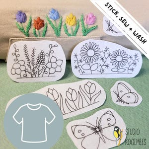 May include: A set of iron-on embroidery patches featuring floral and butterfly designs. The patches are white with black outlines and are ready to be ironed onto fabric. The text "STICK, SEW + WASH" is visible in the upper right corner of the image.
