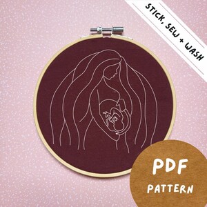 May include: Embroidery hoop with a burgundy fabric background and white embroidery of a pregnant woman holding a baby. The text "STICK, SEW + WASH" is in the top right corner and "PDF PATTERN" is in the bottom right corner.