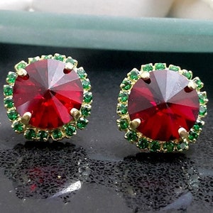 Puede incluir: Un par de pendientes rojos y verdes con una piedra roja redonda y facetada rodeada de un halo de piedras verdes más pequeñas.