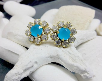 Puede incluir: Un par de pendientes de oro con un centro de piedra preciosa azul rodeado de diamantes de imitación transparentes. Los pendientes tienen forma de flor.
