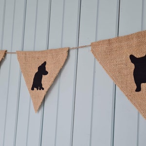 May include: A burlap banner with black silhouettes of dogs. The banner is strung up on a wall and has five flags.