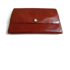 Könnte beinhalten: Eine braune Ledergeldbörse mit einem einzigen Knopfverschluss.